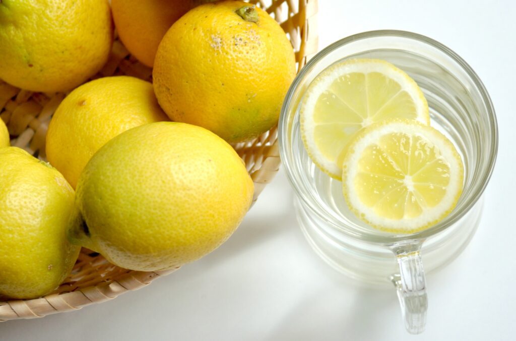 A bowl of lemons next to a glass of lemon water