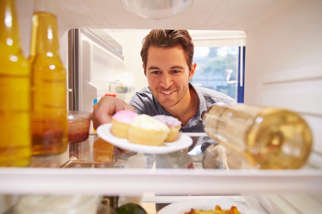 A man reaching for junk food from the fridge