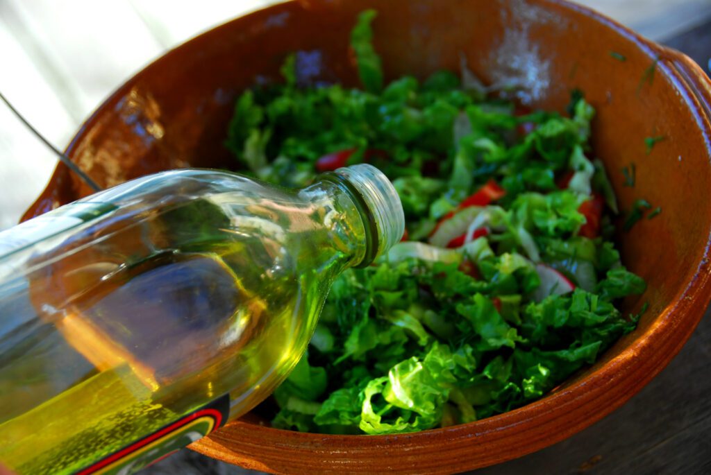 Olive oil being poured over a healthy salad to promote weight loss