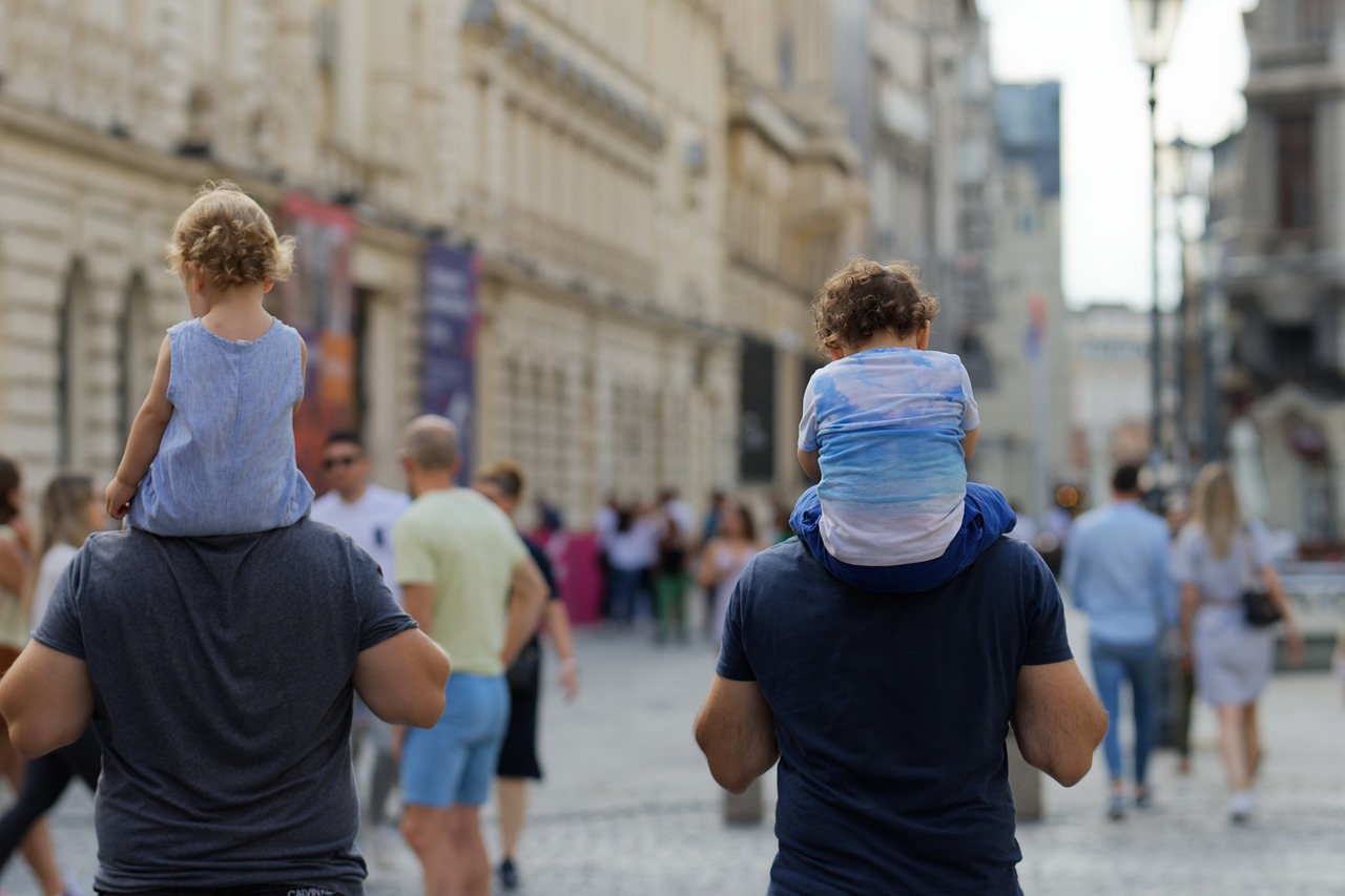 To highlight daily movement, the picture shows people walking down a street, including two fathers carrying their small children.