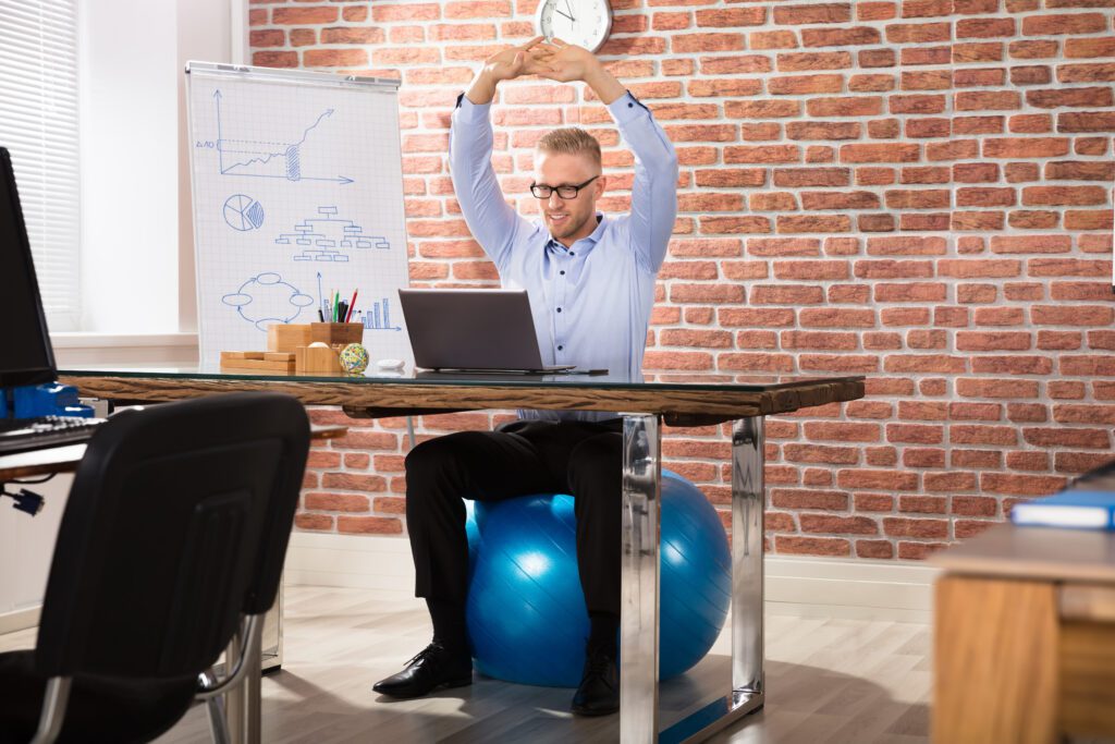 A man at work sitting on an exercise ball while doing stretches.