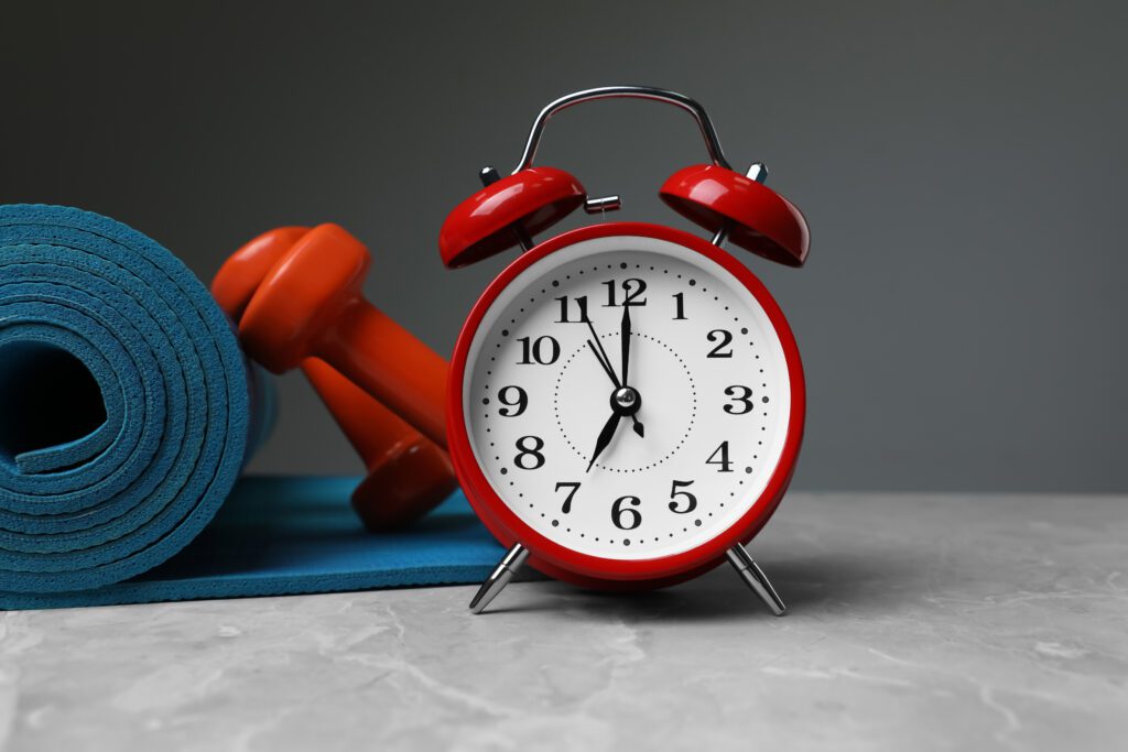 A yoga mat and weights laid out next to an alarm clock.