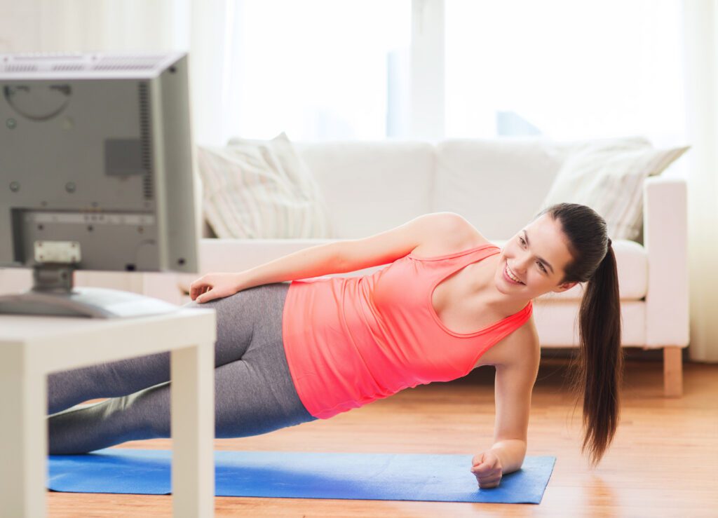 A woman taking an exercise snack by doing a side plank while she watches television. 