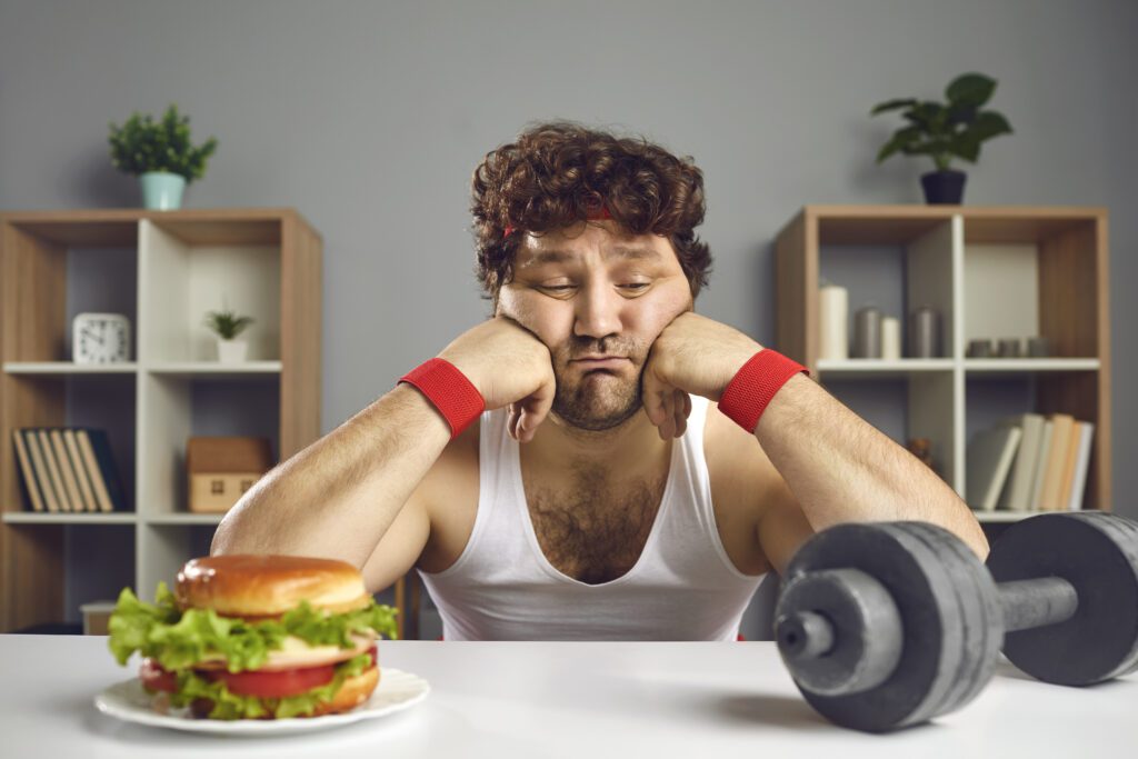 A man using willpower (and struggling) to decide whether to exercise or eat a burger.