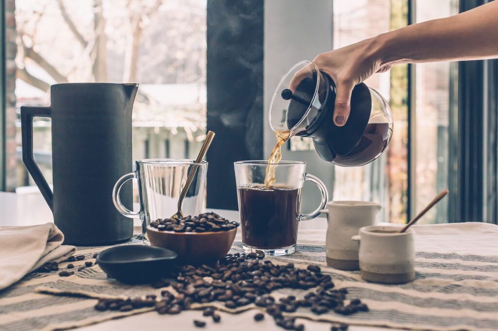 A table with coffee beans and a person pouring a cup of freshly brewed caffeinated coffee.