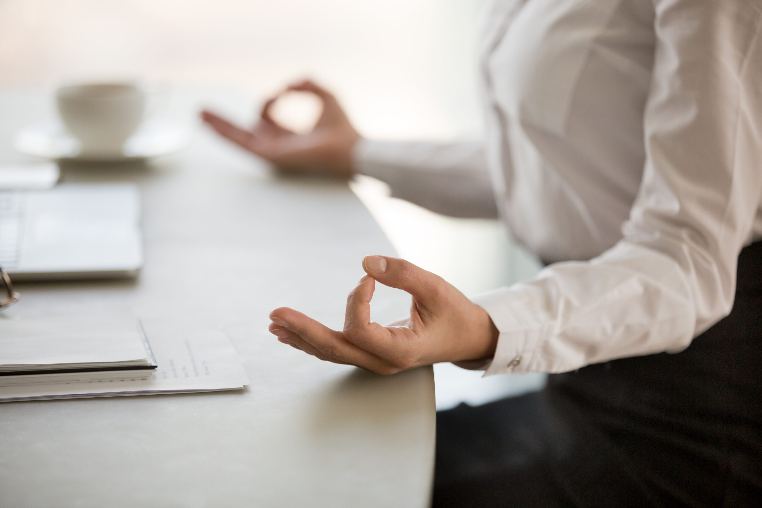 A professionally dressed woman meditating at her desk for stress relief.