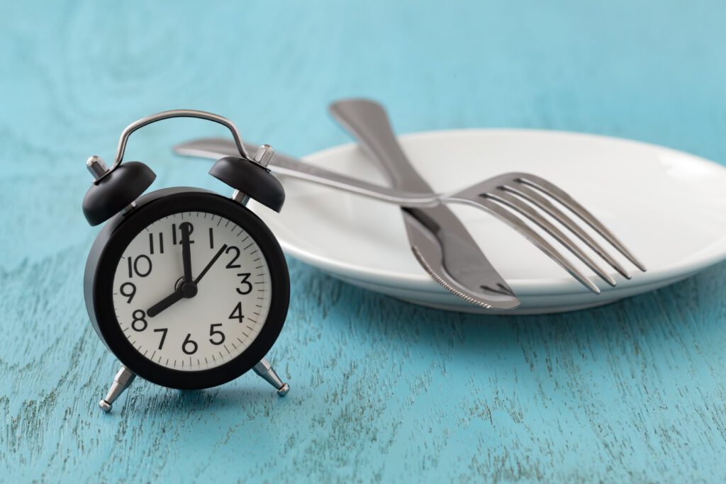 An empty plate next to an alarm clock to highlight exercising before eating breakfast, a type of fasted exercise.
