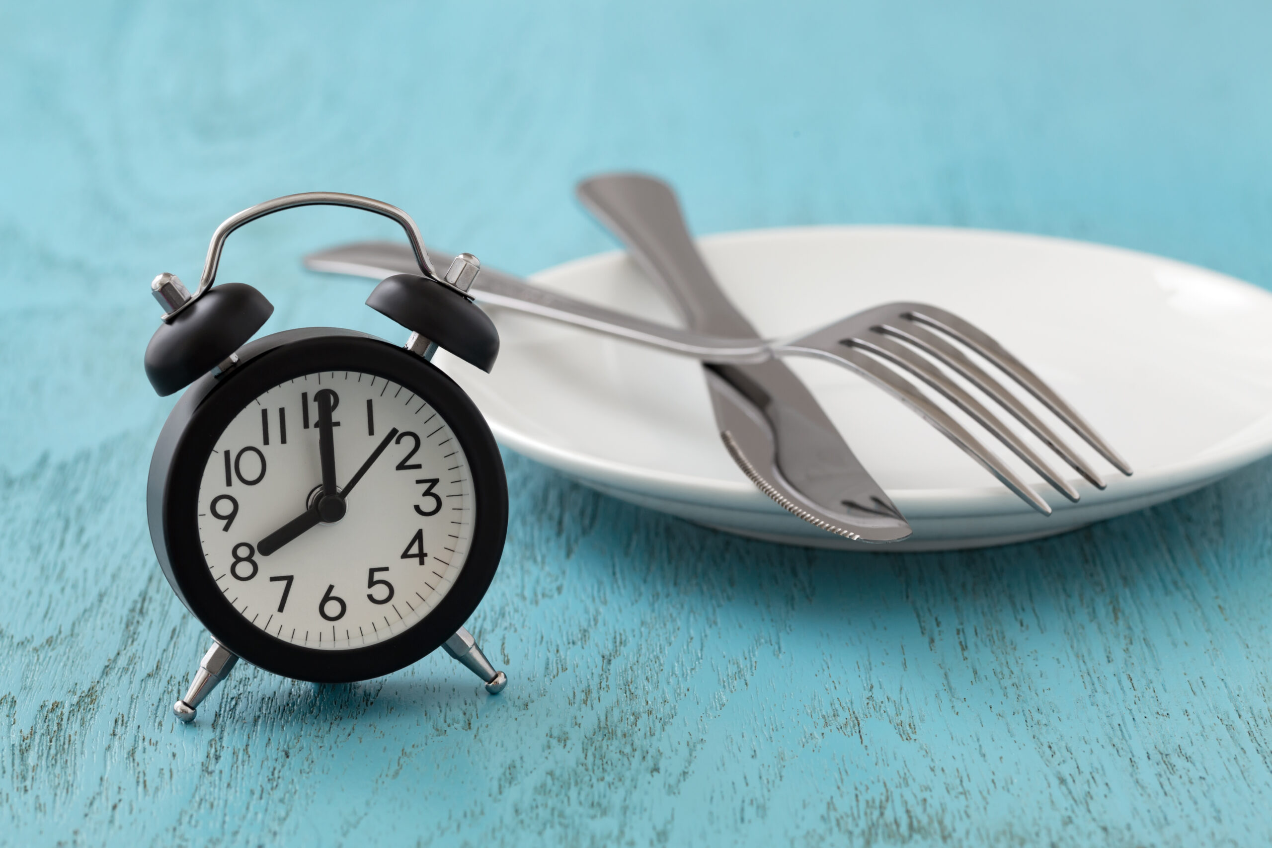 An empty plate next to an alarm clock to highlight exercising before eating breakfast, a type of fasted exercise.