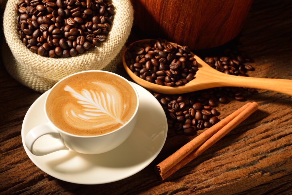 Fresh coffee beans next to a cup of coffee on a small plate.