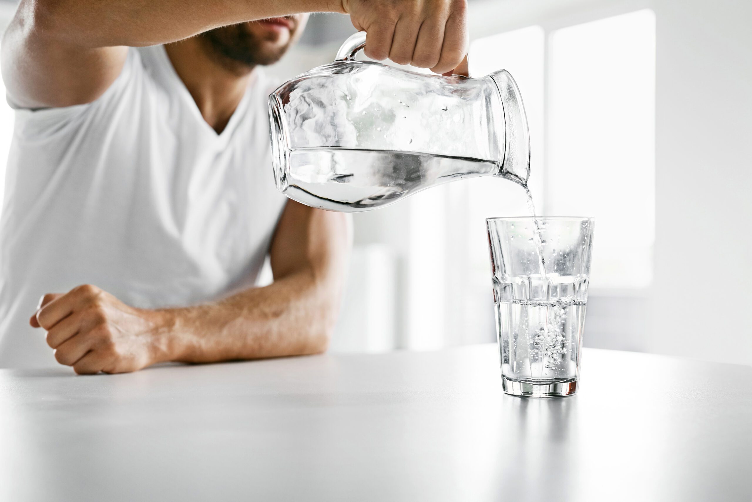 A man pouring himself a glass of water to defeat dehydration.