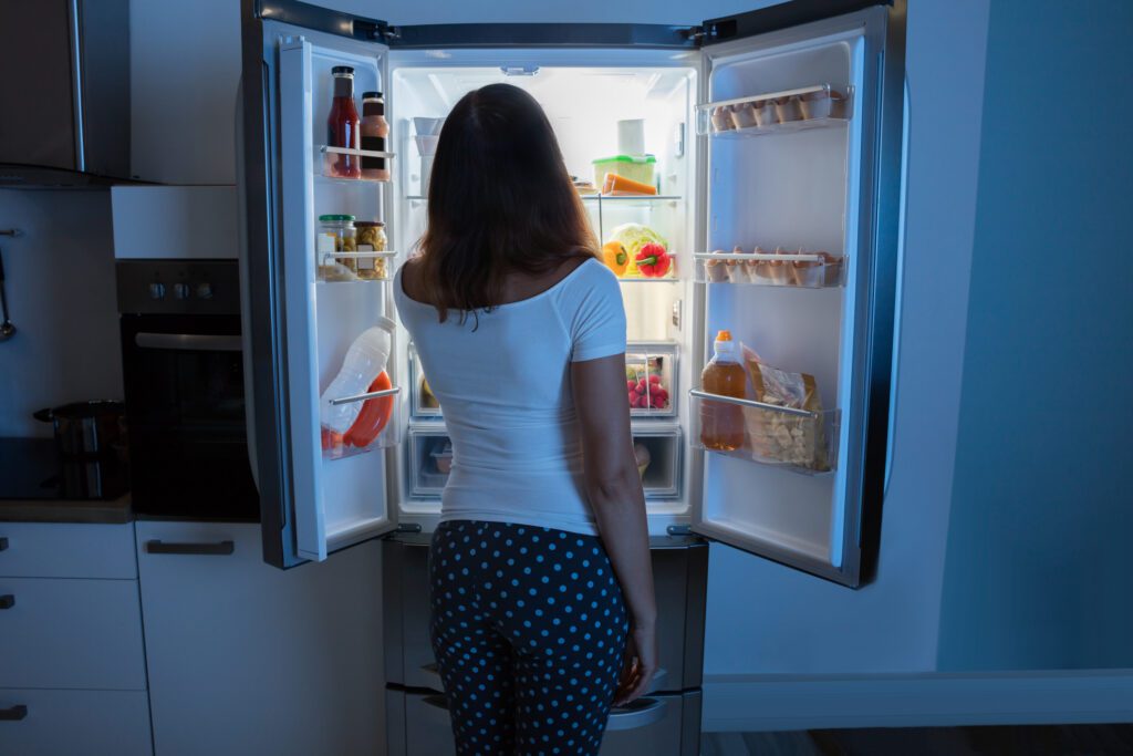 A hungry woman looking in the fridge at night time