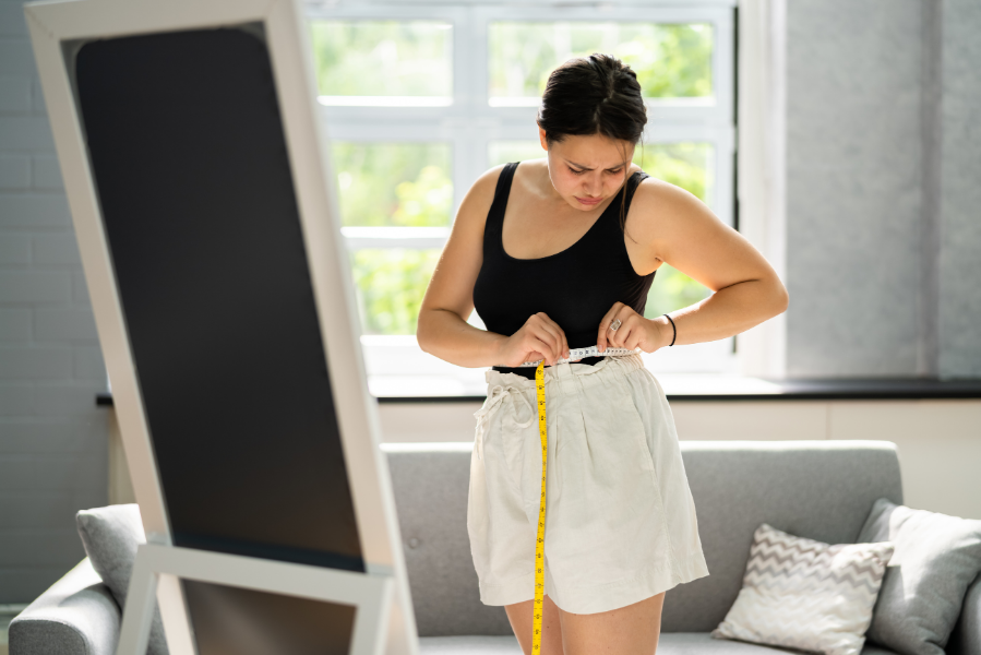 A woman frustratingly measuring her waist, annoyed that her diet is not working.