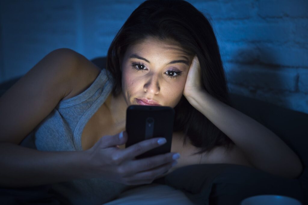 A woman staying up in bed reading her phone.