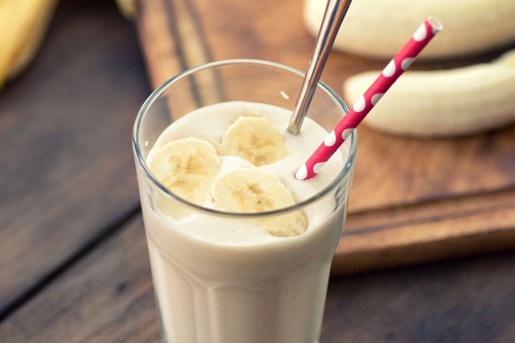 A calorie dense banana smoothie in a glass with a straw